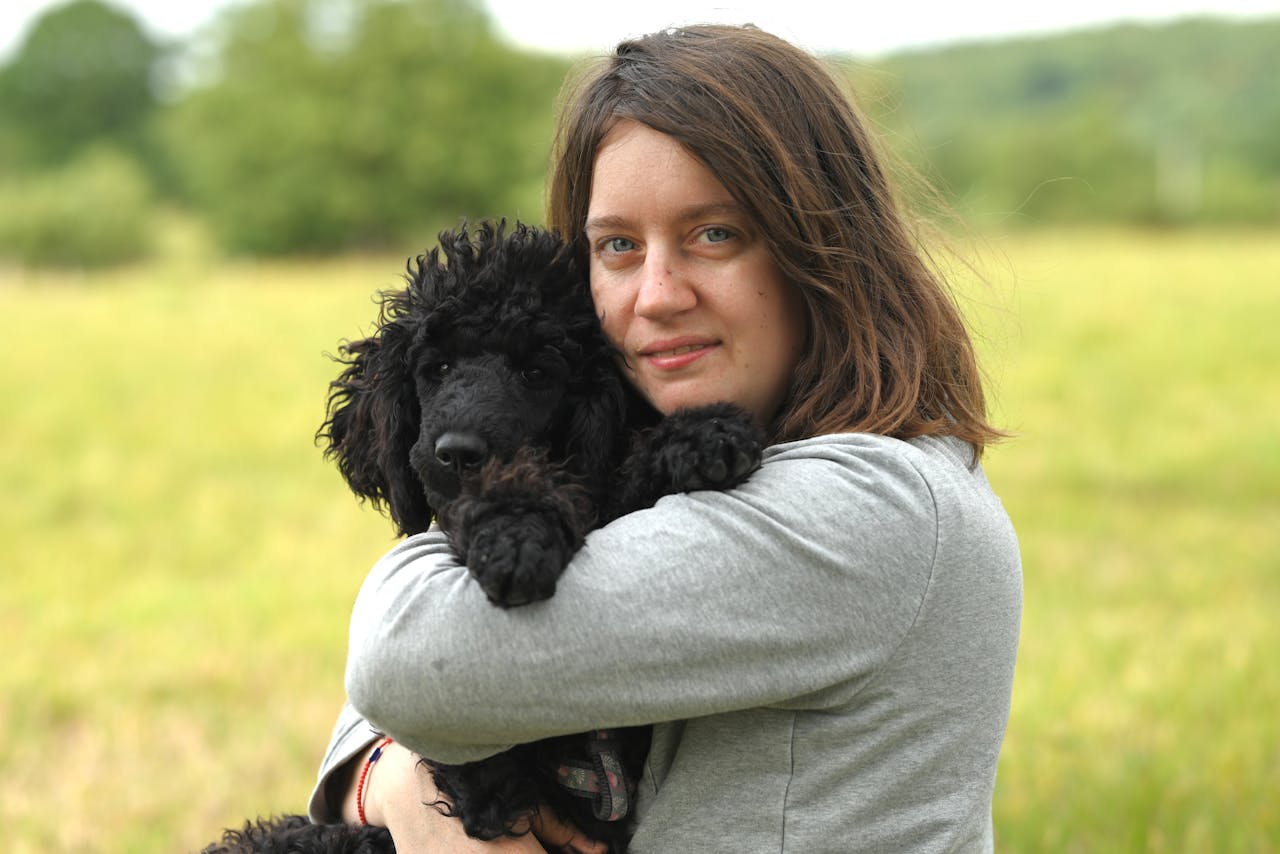 creative A woman lovingly holds her black poodle in a bright, grassy field. Perfect for themes of companionship and outdoor enjoyment.